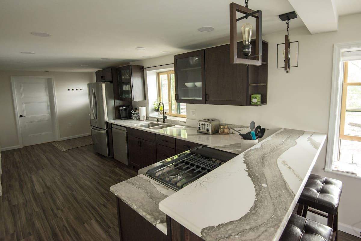 A modern kitchen with dark wood cabinets, a stainless steel refrigerator, a built-in oven, and a large island with a gas stove.