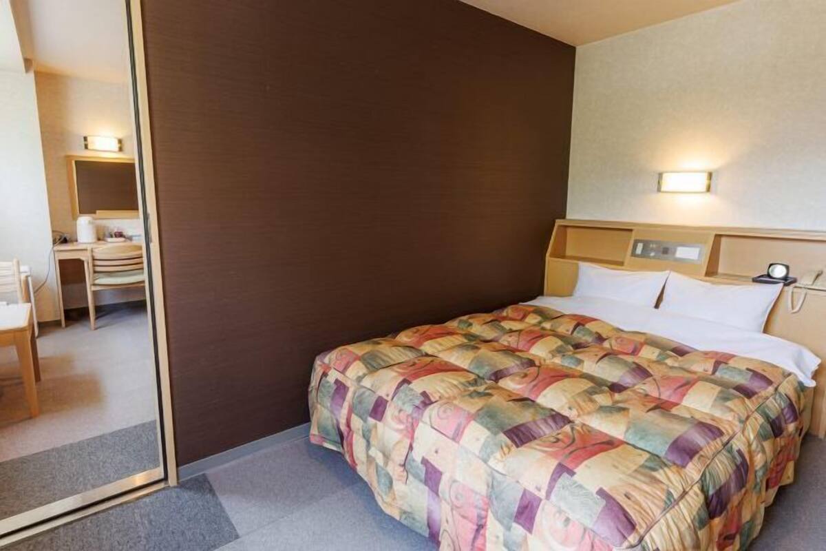 Quarto de hotel com cama, escrivaninha e cadeira.