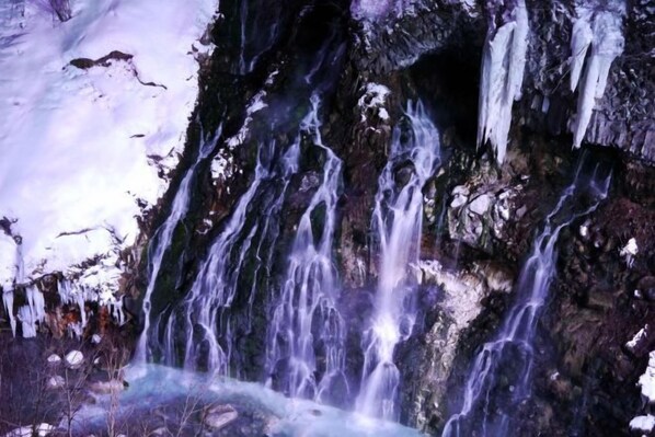 A waterfall cascading over a rocky surface with icicles hanging from the edges. - Biei Shirogane Onsen Hotel Park Hills (Biei)
