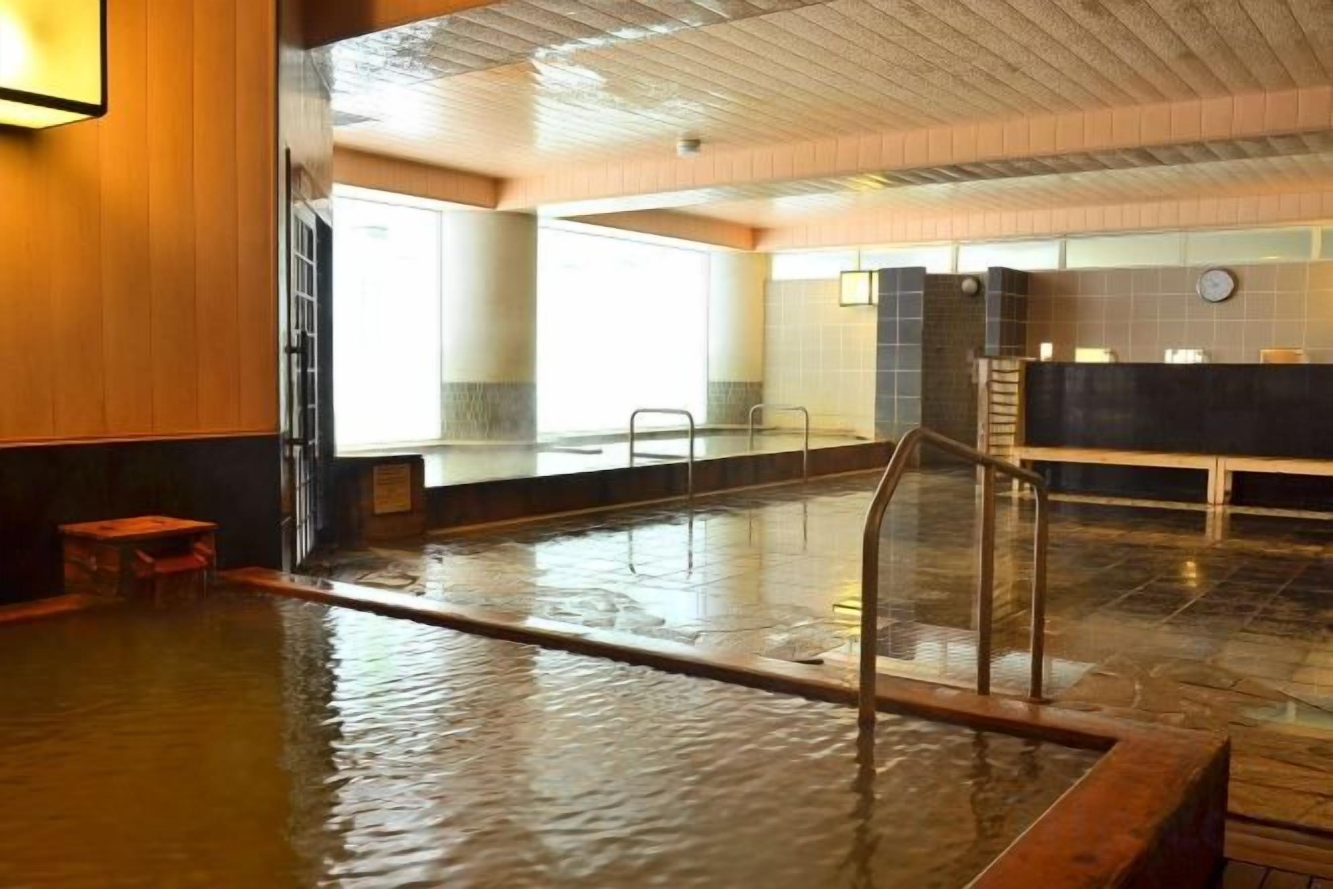 A large indoor swimming pool with a wooden floor, a glass railing, and a reception desk in the background.