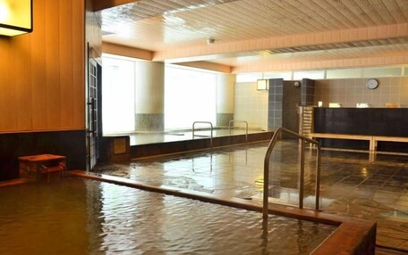 A large indoor swimming pool with a wooden floor, a glass railing, and a reception desk in the background.