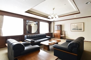 A spacious living room with a large sofa set, a wooden coffee table, and a chandelier. - Biei Shirogane Onsen Hotel Park Hills (Biei)