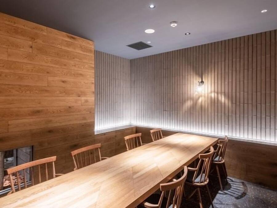A conference room with a long wooden table and chairs, wooden panel walls, and recessed ceiling lights.