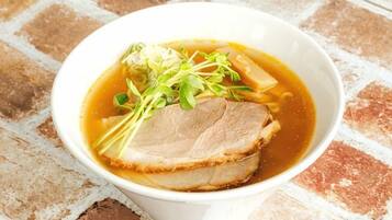 A bowl of soup with a slice of meat and greens on a brick surface.