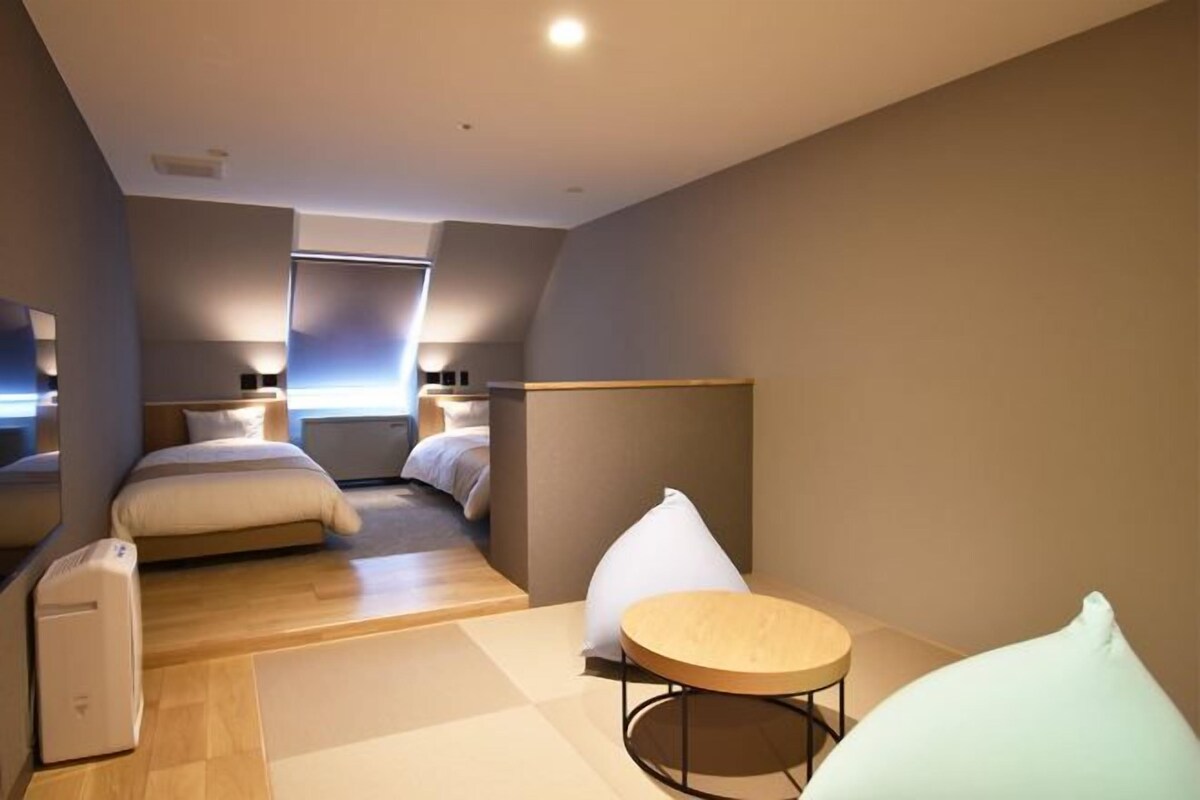 A modern hotel room with a bed, bedside tables, a round table, and a chair.