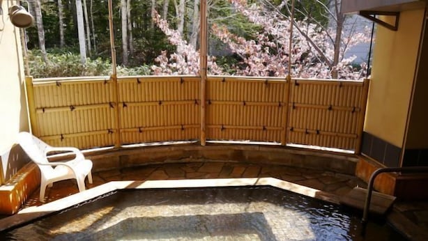 A hot tub with a bamboo fence, a white plastic chair, and a stone floor. - Biei Shirogane Onsen Hotel Park Hills (Biei)