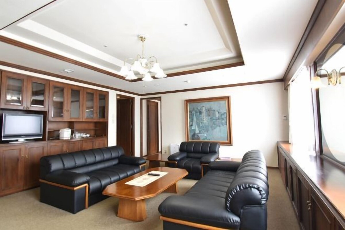 A spacious living room with a large sofa set, a television, and wooden cabinets.