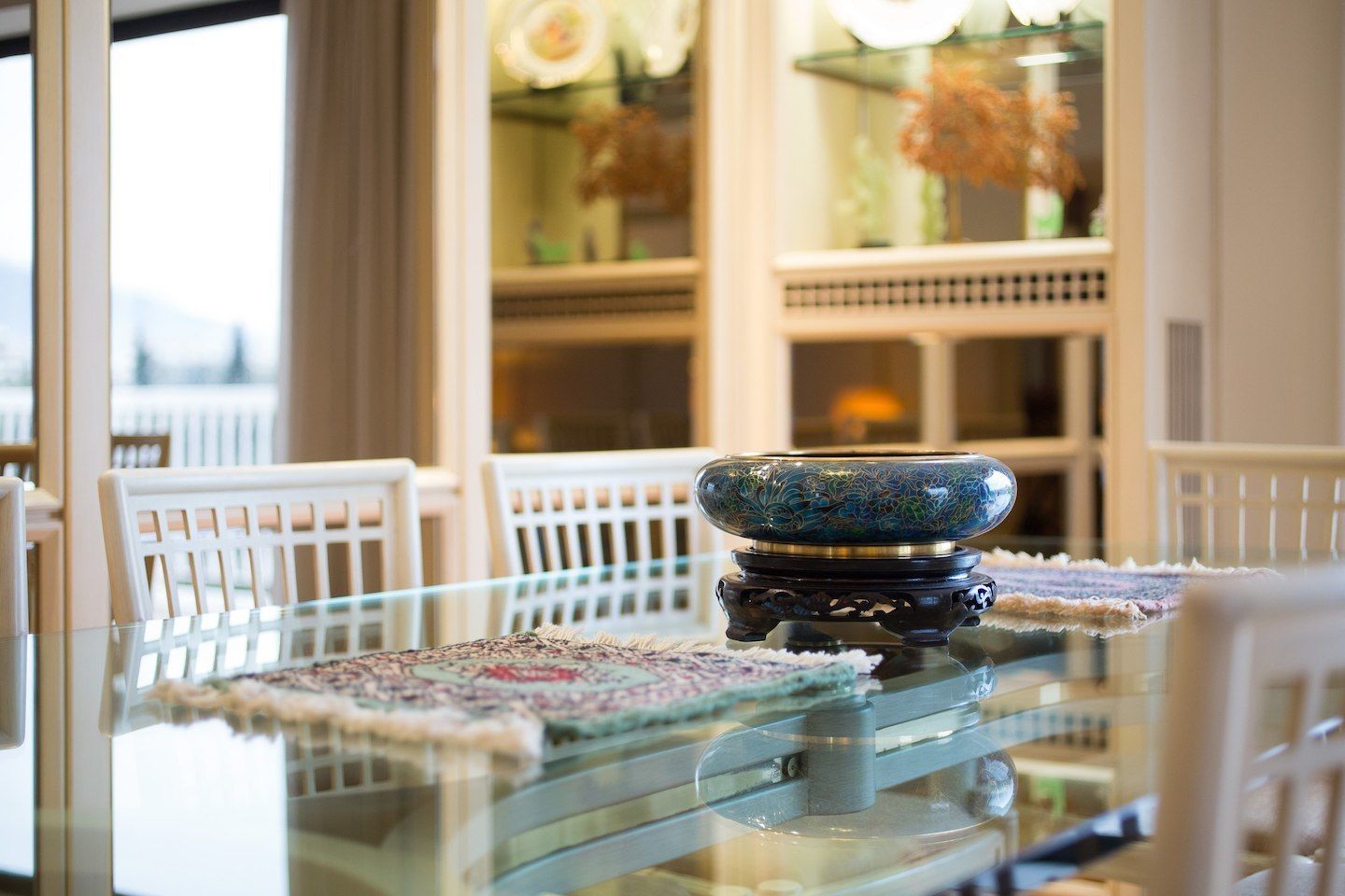 Una mesa de comedor con cubierta de vidrio, un cuenco decorativo y un mantel individual estampado.