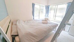 A bedroom with a bed, a window with curtains, and a small stool with towels.