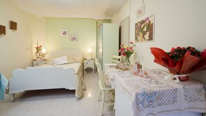 A bedroom with two beds, a dining table with a floral tablecloth, and a vase of flowers. - ERATO  APARTMENT  IN ARGOSTOLI (Argostoli)