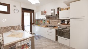 Una cocina moderna con armarios blancos, estufa a gas, horno empotrado y cafetera.