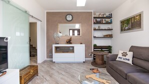 Una sala de estar moderna con un mueble blanco para entretenimiento, un sofá marrón, una mesa de centro de vidrio y un cojín con motivos de mascotas.