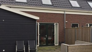 Ein Haus mit geneigtem Dach, Solaranlagen, einer Garage und einem eingezäunten Garten mit Stühlen.
