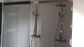 Eine moderne Dusche mit Glasabtrennung, einer Handbrause und einem wandmontierten Wasserhahn.