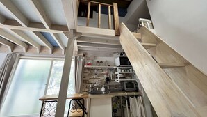 A loft-style room with exposed wooden beams, a kitchen area with appliances, and a window with curtains. - Home WIFI & Compact & Tranquil Apt with LOFT! (Tokyo)