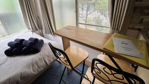 A hotel room with a bed, a small table, two chairs, and a window with a view of trees and a fence. - Home WIFI & Compact & Tranquil Apt with LOFT! (Tokyo)