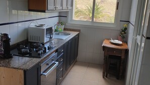 A compact kitchen with a gas stove, microwave, and sink. There is a window providing a view of the outdoors. - Luxury apartment in Los Alisios (Santa Cruz de Tenerife)