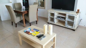 A living room with a TV, a wooden coffee table with magazines and remote controls, a dining table with chairs, and a white entertainment unit with shelves. - Luxury apartment in Los Alisios (Santa Cruz de Tenerife)