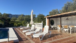 Ein Poolbereich mit Liegestühlen, einer überdachten Lounge und Blick auf Berge.