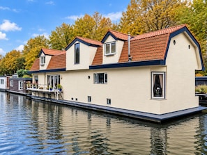 Une maison située au bord de l’eau, avec un toit recouvert de tuiles rouges, un balcon et une jetée qui s’avance dans l’eau.