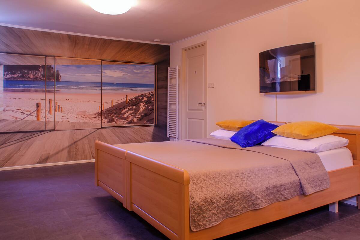 A bedroom with a bed, a mirror, and a beach mural on the wall.