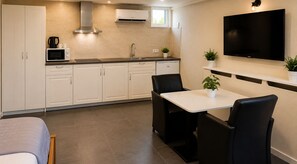 Une cuisine compacte avec un coin repas, des meubles blancs, un four à micro-ondes encastré et un téléviseur à écran plat.