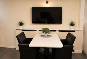 A dining area with a table and chairs, a flat-screen TV mounted on the wall, and two potted plants on either side of the TV. - B&B Hotel Elselina (Schiedam)