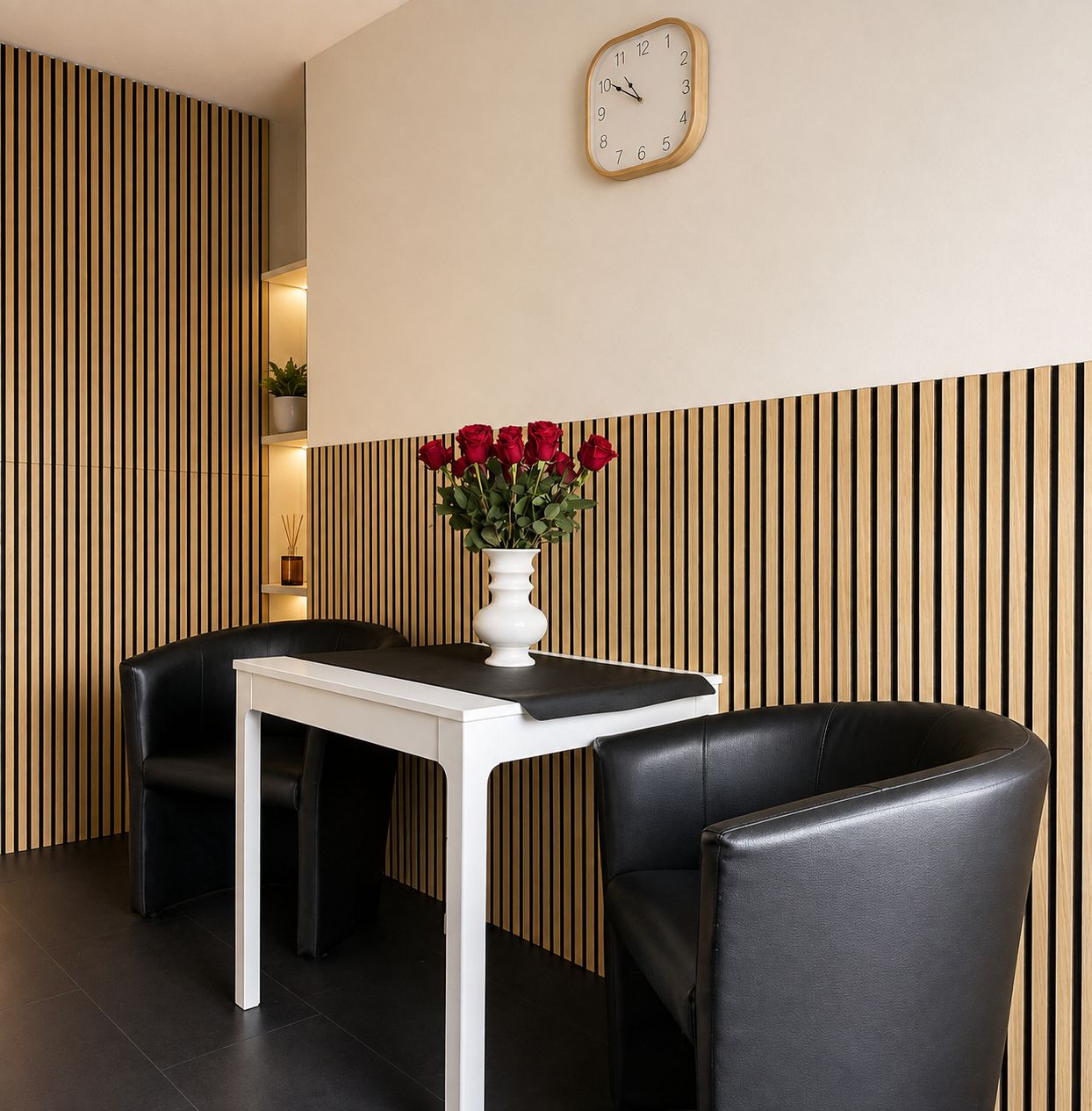 A modern room with a white table and black chairs, a clock on the wall, and a vase with red roses.