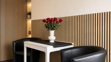 A modern room with a white table and black chairs, a clock on the wall, and a vase with red roses.