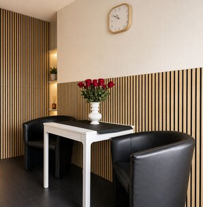 A modern room with a white table and black chairs, a clock on the wall, and a vase with red roses.