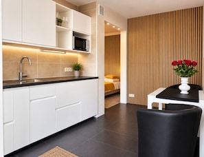 A modern kitchen with white cabinets, a black countertop, and a microwave. There is a dining area with a black chair and a white table. - B&B Hotel Elselina (Schiedam)
