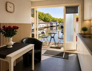 A modern kitchen with a view of a canal, a dining area with a table and chairs, and a clock on the wall. - B&B Hotel Elselina (Schiedam)