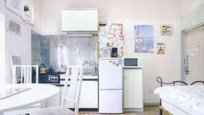 Una cocina compacta con estufa, refrigerador y microondas. Hay una mesa de comedor con sillas y una cama con colcha estampada.