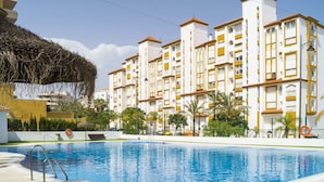 A swimming pool surrounded by a multi-story building with balconies, palm trees, and a clear sky. - Nice apartment for 4 guests with A/C, pool, WIFI, TV and terrace (Estepona)