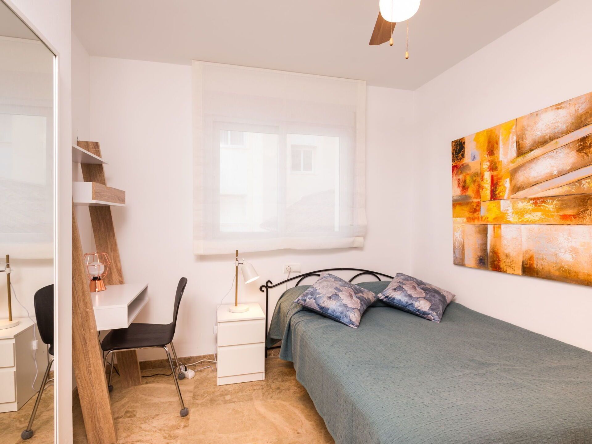 A bedroom with a bed, a desk, a chair, a window, and a wall art piece.