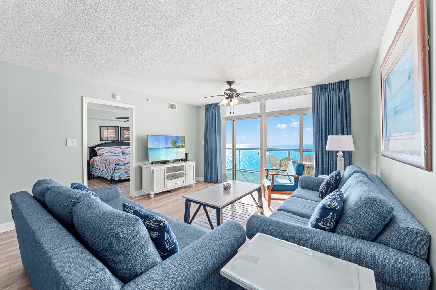 Una sala de estar moderna con un conjunto de sofá, una televisión y un balcón con vista al mar.