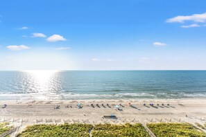 A beach with a clear sky, calm sea, and a sandy area with some structures and people. - Clean Oceanfront Condo, Free Wifi, Lazy River | Crescent Keyes - 1208 (North Myrtle Beach)