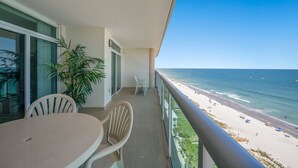 A balcony with a view of the beach, a table, two chairs, and a potted plant. - Clean Oceanfront Condo, Free Wifi, Lazy River | Crescent Keyes - 1208 (North Myrtle Beach)