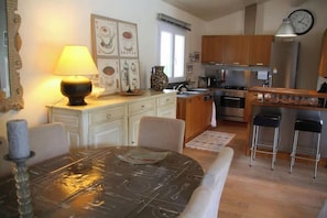 A dining area with a table, chairs, a lamp, and a kitchen in the background. - Comfortable house with pool G0269 (Lacanau)