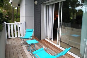 Una terraza de madera con dos sillones azules y un ventanal que da a una habitación.