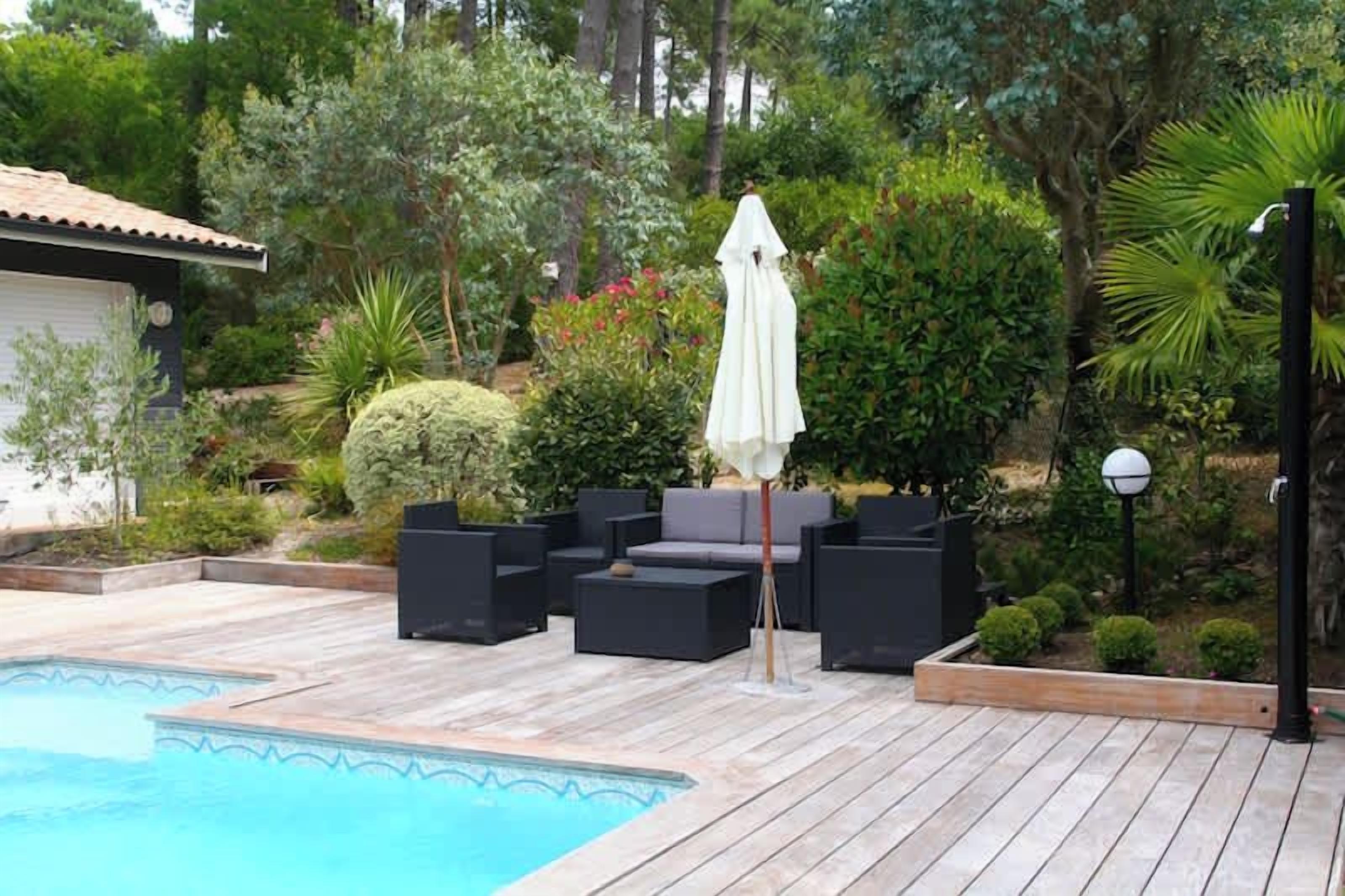 A poolside area with a wooden deck, black outdoor furniture, and a white umbrella.