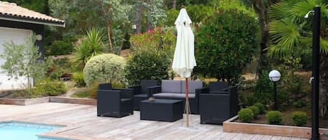 A poolside area with a wooden deck, black outdoor furniture, and a white umbrella.