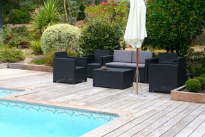 A poolside area with a wooden deck, black wicker furniture, and a white umbrella. - Comfortable house, big pool with wooden terrace, ideal location (Lacanau)