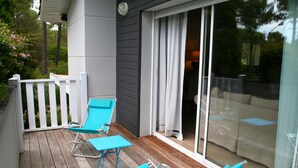 A wooden deck with blue lounge chairs and a glass door leading to a covered patio area. - Comfortable house, big pool with wooden terrace, ideal location (Lacanau)
