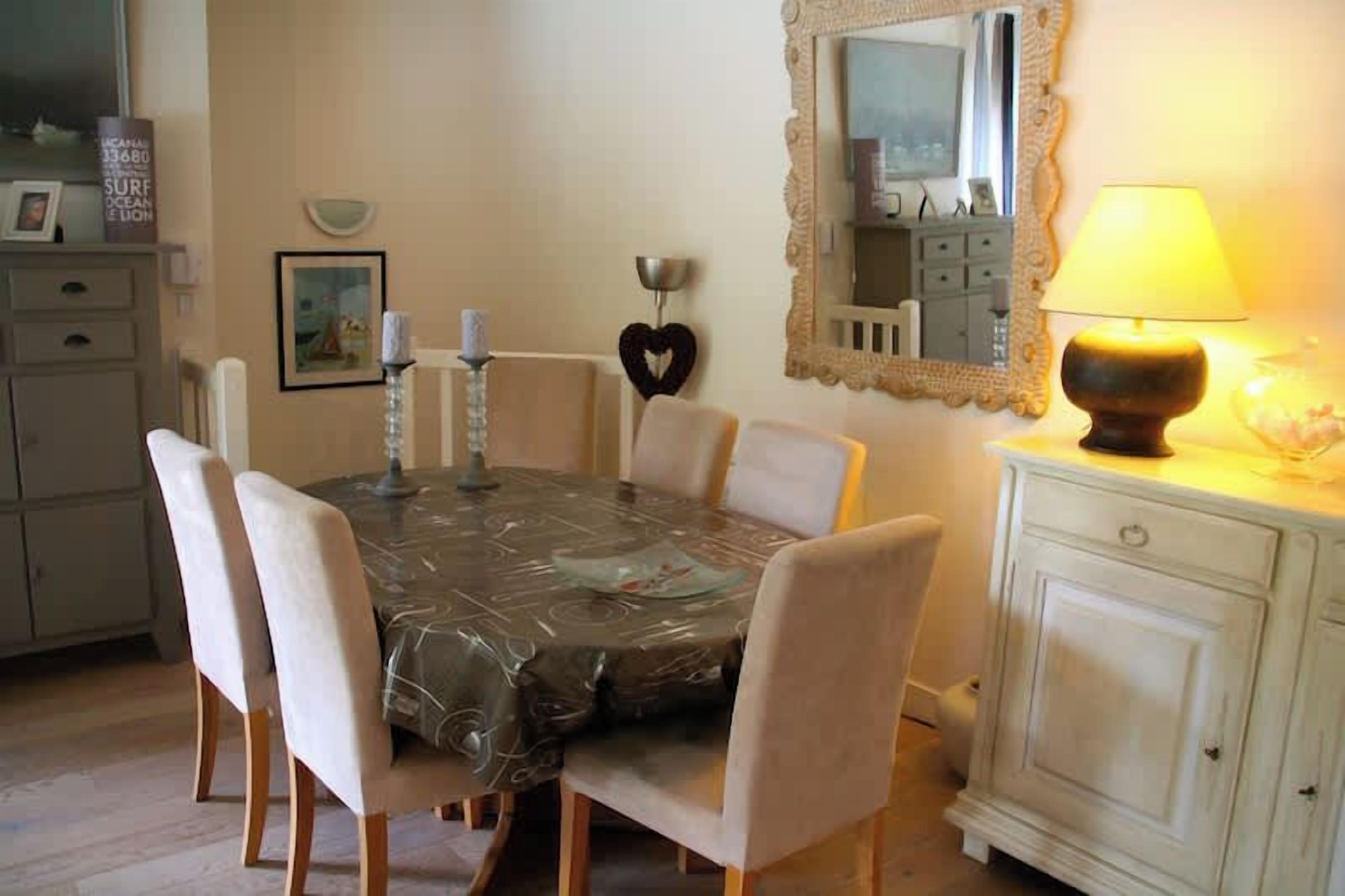 A dining area with a table covered in a patterned tablecloth, surrounded by chairs.