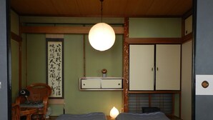 Een traditionele Japanse kamer met twee bedden, een houten tafel, een hanglamp en een kalligrafiewerk aan de muur.