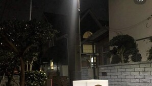 Bordje van een vakantiehuis met een goed verlichte ingang en een bakstenen muur op de achtergrond.