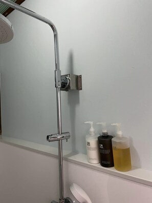 A bathroom with a shower, a toilet, and a shelf with three bottles of liquid.