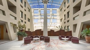 A spacious atrium with a high ceiling, multiple seating areas, and large potted plants.