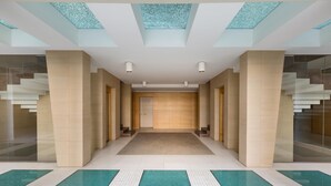 A modern hotel lobby with a central staircase, glass walls, and a patterned floor.
